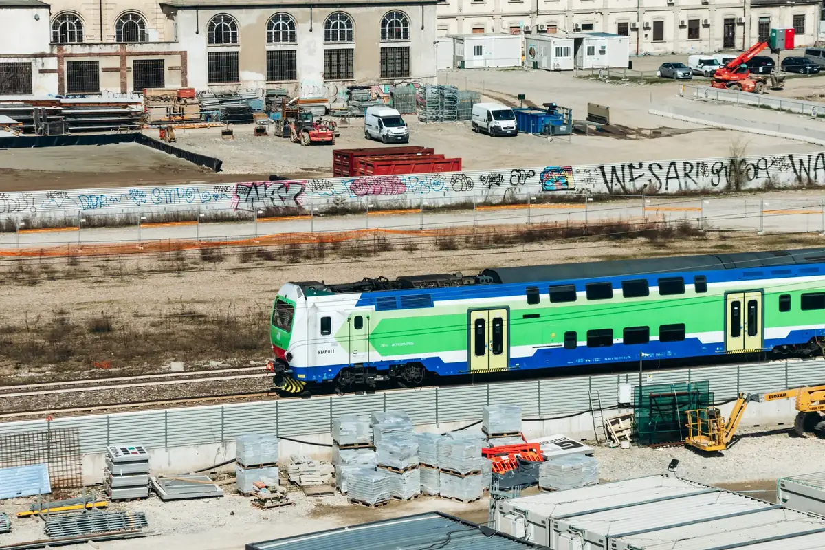 Milan, Italy – March 19, 2025 : Trenord train passing construction site of Olympic Village near Fondazione Prada