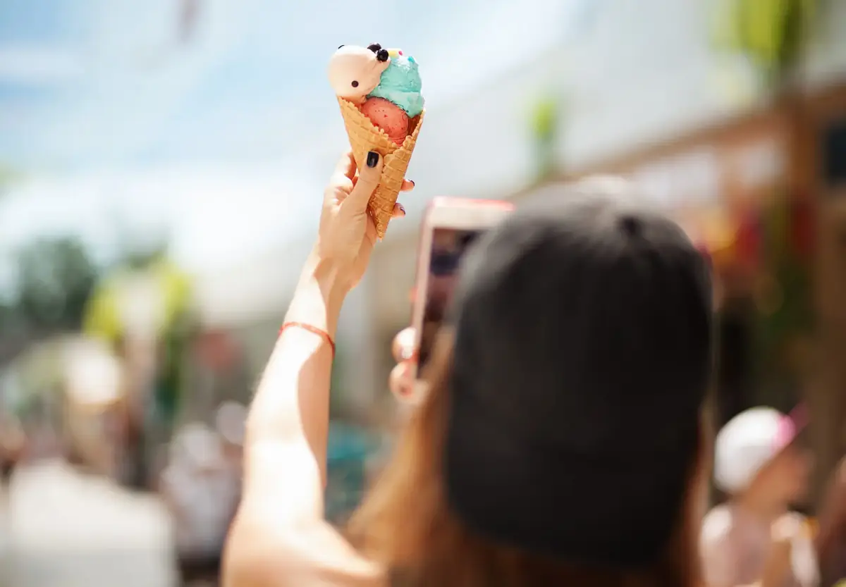 Pretty girl taking picture of ice cream on smartphone. Focus on ice cream